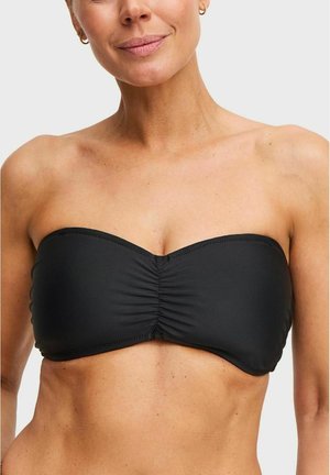 Vrouw die een zwarte, strapless bandeau-bikinibovenstuk draagt, met blote schouders en bovenlichaam tegen een effen achtergrond.
