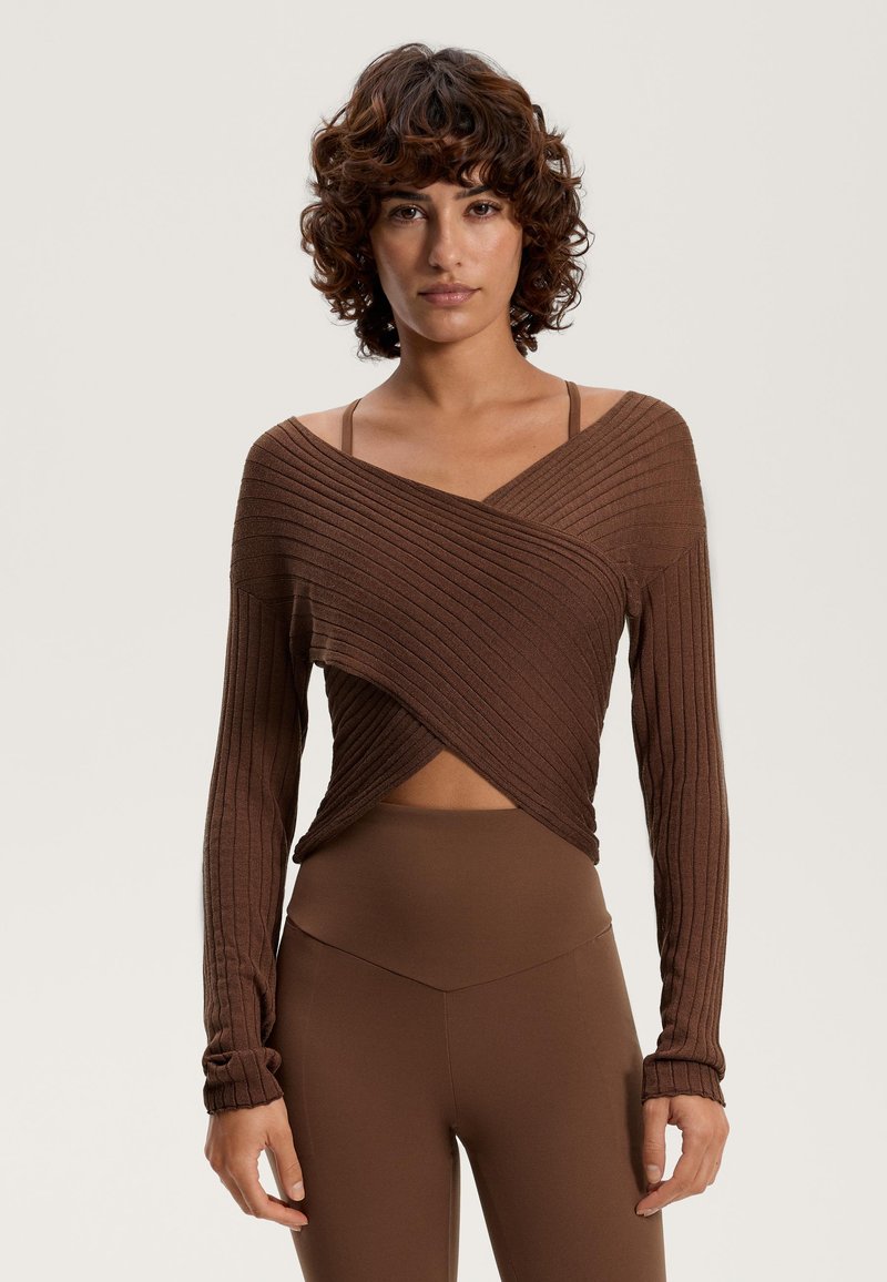 Barna bordázott, hosszú ujjú felső, lecsúszott vállú kialakítással, keresztezett aljjal. Magas derekú leggings-szel párosítva.