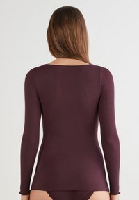 Langarmshirt aus dunkelburgunderfarbenem Stoff, mit rundem Halsausschnitt und figurbetontem Schnitt, glatter Textur und minimalen Nähten.