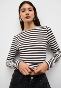 Långärmad topp med växlande bruna och vita ränder, rund halsringning och en figurnära silhuett, kombinerad med högmidjade svarta byxor.