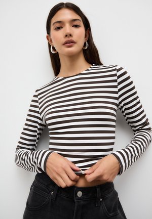 Langärmeliges Oberteil mit abwechselnd braunen und weißen Streifen, einem runden Ausschnitt und einer figurbetonten Silhouette, kombiniert mit hoch taillierten schwarzen Hosen.