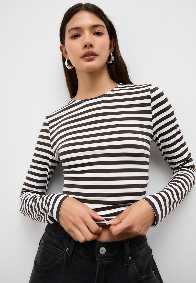 Långärmad topp med växlande bruna och vita ränder, rund halsringning och en figurnära silhuett, kombinerad med högmidjade svarta byxor.