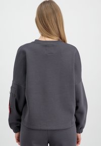 Sweatshirt gris foncé avec des manches longues, col rond côtelé et une poche sur la manche gauche. Texture de tissu lisse.