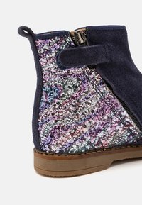 Mørkeblå suede ankelstøvlett med en glitrende, flerfarget paljettpanel, med glidelås på siden og en brun gummisåle.