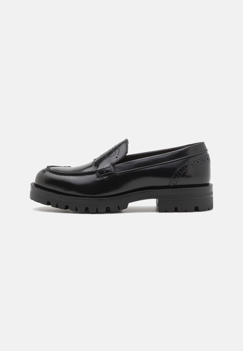 Mocassin en cuir noir avec semelle en caoutchouc épaisse et perforations brogue discrètes, profil latéral sur fond uni.