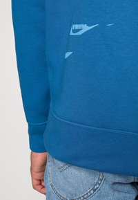 Felpa blu con finitura testurizzata, dotata di un logo Nike azzurro sulla parte bassa della schiena. Completata con polsini e orlo a coste.