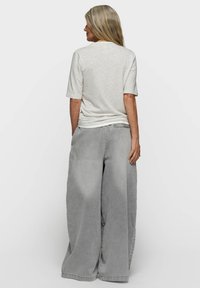 Pantalon denim gris clair surdimensionné avec une coupe ample et un tissu texturé. Associé à un haut beige à manches courtes, vu de dos.