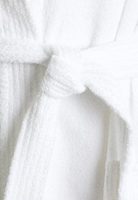 White terry cloth robe with textured stripes, featuring a tied belt and loose fit. Soft, absorbent material with a plush finish.