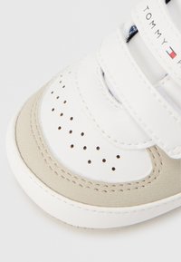 Λευκό δερμάτινο αθλητικό παπούτσι με μπεζ λεπτομέρειες, διαθέτοντας οπές, ιμάντες με βέλκρο και λογότυπο Tommy Hilfiger κοντά στη φτέρνα.