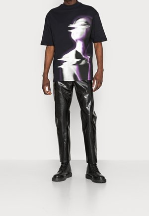 Black oversized t-shirt with a graphic design in purple and grey. Paired with black textured leather pants and black lace-up boots.
