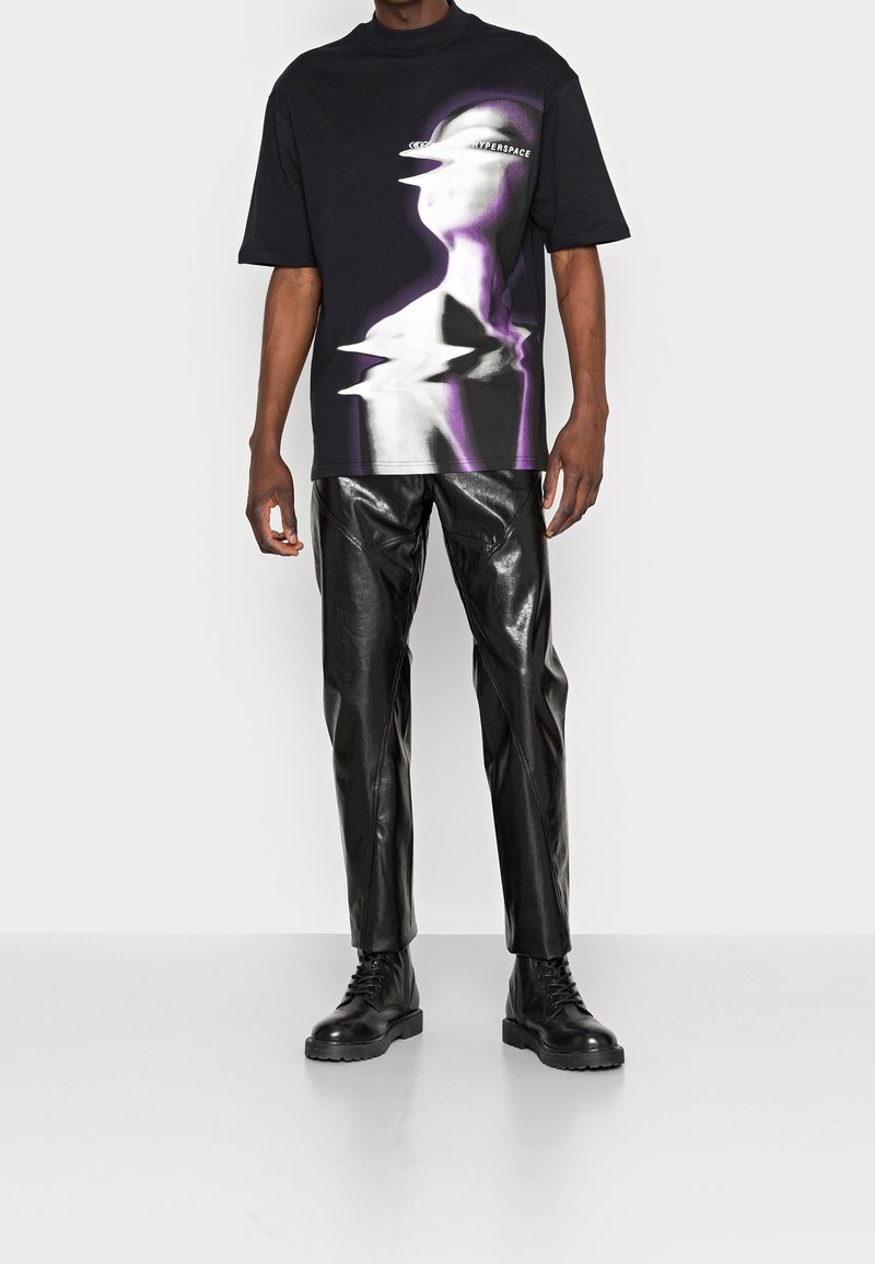 T-shirt noire oversize avec un design graphique en violet et gris. Associé à un pantalon en cuir texturé noir et des bottes noires à lacets.