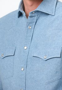 Lichtblauwe denimen overhemd met een button-down kraag, zilveren drukknoopjes en twee voorkeuzes met spitse kleppen en een gestructureerd oppervlak.