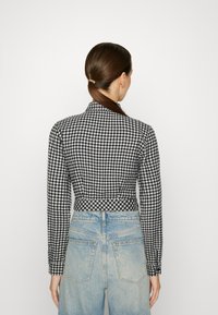 Dlouhý rukáv, černobílá kostkovaná košile s vysokým límcem, přiléhavý střih a knoflíkové manžety, spárovaná s vysokým pasem a světlými denimovými džíny.