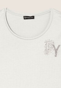 Camiseta blanca de manga corta con cuello redondo, que presenta detalles de pedrería plateada que deletrean "FY" en el lado izquierdo. Textura de tela suave.