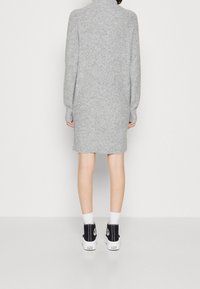 Grå stickad klänning med hög krage, långa ärmar och avslappnad passform, i kombination med svarta högtoppsskor och vita strumpor.