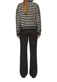 Schwarz-weißer karierter Cardigan mit strukturiertem Strick, geripptem Saum und Bündchen. Kombiniert mit schwarzen Schlaghosen, von hinten gesehen.