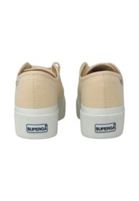 Sneakers in tela beige con suole in gomma bianca, forma arrotondata e un piccolo logo sul tallone. Presentano una suola testurizzata per una maggiore aderenza.
