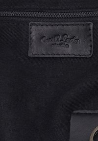 Tissu noir avec une fermeture éclair horizontale au-dessus d'une étiquette en cuir noir cousue embossée de "Quiz! Ladies studio".