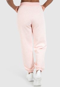 Lichtroze sweatpants gemaakt van zachte stof; met een elastische tailleband, taps toelopende manchetten en zijzakken. Draagt met witte sportschoenen.