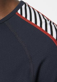 Camiseta atlética en color navy con una tela texturizada, acentos en blanco y negro a rayas en los hombros y ribetes rojos a lo largo de las costuras.