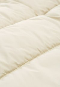 Edredón acolchado color beige claro con una textura suave y un patrón cosido, que presenta secciones espaciadas de manera uniforme y un acabado suave.