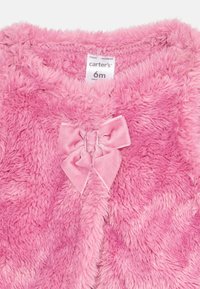 Giacca per neonato rosa fuzzy con una texture morbida, caratterizzata da un grande fiocco in velluto rosa al centro e un'etichetta che indica la taglia di 6 mesi.