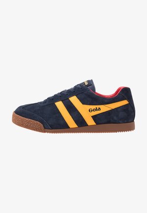 Marineblaues Wildleder-Sneaker mit gelben diagonalen Streifen, strukturiertem braunem Gummisohle und rotem Innenraum. Mit markiertem Logo an der Seite.