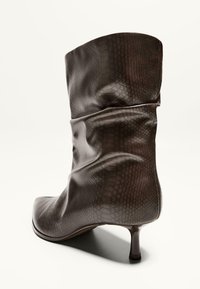 Botină din piele maro, cu un model texturat în stil piele de șarpe, design conic și toc subțire. Finisaj moale, pliat, în partea superioară.