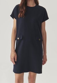 Navy blue short-sleeve dress with a straight cut, featuring two front pockets with gold buttons, made from a smooth fabric.