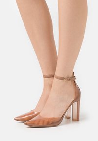 Průhledné lodičky s špičatou špičkou, hnědým kotníkovým páskem a průhledným blokovým podpatkem, s hladkým a lesklým povrchem.