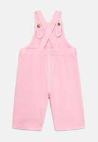 Rosa todler jumpsuit med justerbare kryssede stropper og knappeåpninger på en enkel hvit bakgrunn.