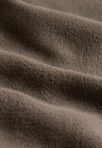 Ruda, švelni ir tekstūruota vilnos medžiaga su švelniais raukšlėmis ir klostėmis, rodanti spalvų variacijas dėl šviesos.