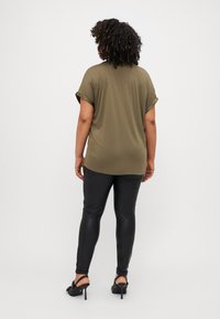 Maglietta verde oliva a maniche corte con risvolti, abbinata a leggings neri lucidi e scarpe alte nere. Design semplice e comodo.