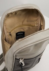 Plecak z beżowymi i czarnymi sekcjami, o gładkiej teksturze, złotą kieszenią na suwak oraz etykietą na beżowym podszewce.