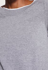 Harmaa huppari, jossa on pyöreä pääntie, sileä pinta ja kontrastivärinen valkoinen trimmi kauluksessa. Yksinkertainen ja rento muotoilu.