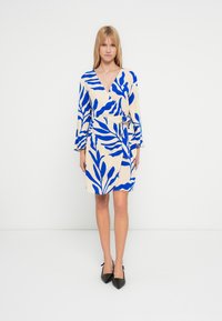 Rochie tip petrecută crem cu modele îndrăznețe de frunze albastre. Are mâneci lungi, decolteu adânc în V și talie legată pentru o siluetă bine conturată.