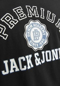 Čierne bavlnené tričko so výrazným bielym a svetlomodrým textom "PREMIUM JACK & JONES" a okrúhlym logom s nápisom "DENIM ACADEMY SINCE 1990."