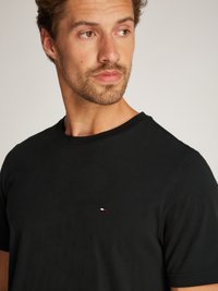 Black cotton t-shirt with short sleeves featuring a small red, white, and blue logo on the left chest. Smooth texture, classic crew neckline.