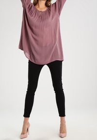Lys lilla bluse med rund halsudskæring og nøglehul detalje, parret med sorte skinny jeans og lyserøde højhælede sko. Glat, flydende stoftekstur.