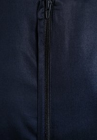 Marinfärgad tyg med en slät struktur har en central dragkedja. Dragkedjan är svart, vilket kontrasterar subtilt mot tygfärgen.