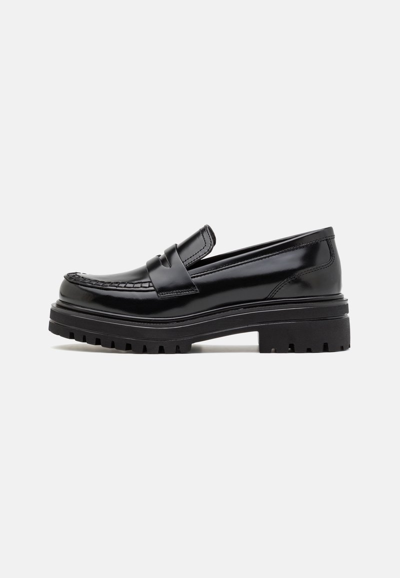 Mocassin en cuir noir brillant avec semelle épaisse rainurée et détail de bout mocassin cousu, vu de profil sur un fond uni.