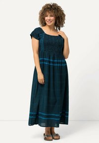 Maxi-mekko tummansinisenä turkoosilla kuvioinnilla, kootun vartalon yläosalla, lyhyillä hihoilla ja liehuvalla hameella. Yhdistetty harmaisiin sandaaleihin.