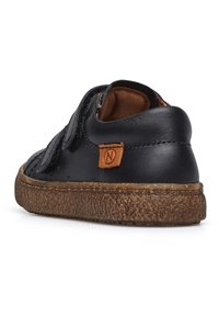 Scarpa in pelle nera con suola texturizzata marrone, dotata di cinturino in velcro e patch con logo in beige sul tallone. Superficie liscia con una leggera trama.