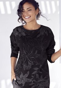 Sweatshirt noir avec un motif floral subtil, col rond et manches longues. Le tissu semble doux avec une coupe décontractée.