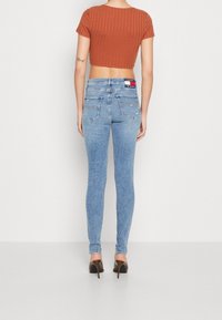 Jeans de denim ajustados de color azul con un lavado claro, dos bolsillos traseros y un parche de marca en la cintura. Combinados con un top corto de color óxido.