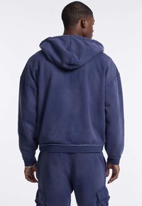 Navyblauwe hoodie met een cropped ontwerp, losse pasvorm en een ruwe zoom. Beschikt over een zachte textuur en verlaagde schouders.