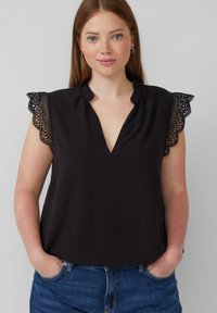 Haut sans manches noir avec des accents en dentelle sur les épaules, un décolleté en V et une coupe décontractée, accompagné de jeans bleus.