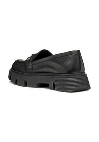 Zapato de cuero negro con una suela de goma gruesa, que presenta una puntera redondeada y acentos decorativos. La parte trasera tiene un detalle acanalado vertical.