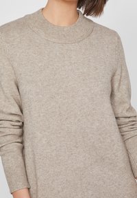 Maglione beige lavorato a maglia con colletto rotondo a coste e maniche lunghe. Texture morbida, design casual e vestibilità leggermente rilassata.
