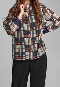 Checked blouse in lightweight fabric featuring cream, navy, red, and black colors. It has a buttoned front and roll-up sleeves.